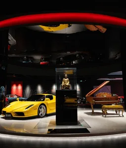 A well-lit showroom filled with various vehicles, including sports cars and a motorcycle, and modern furniture, with a focus on luxury and sophistication