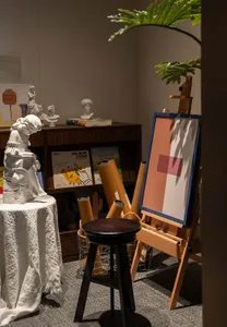 Cozy living space with a wooden floor, a white table, a painting, a statue, and a bookshelf with several books