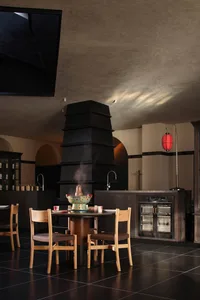 A dimly lit restaurant dining area with a wooden table and chairs, a fireplace, and a warm atmosphere