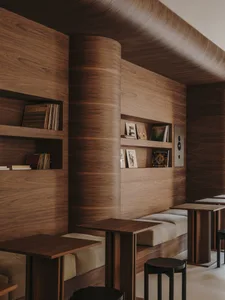 A warm and cozy restaurant with wooden walls and a wooden table, featuring books and a reading area