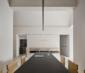 A large, open dining room with a modern design, white walls, and soft lighting, featuring a dining table and chairs, and a vase on the table
