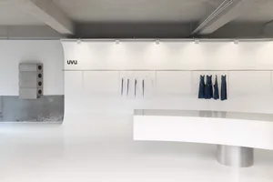 白色地板的簡潔零售空間中，中央柜台和周圍的架子，展示多件衬衫