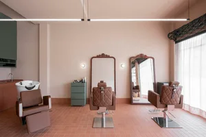 A clean and well-maintained hair salon with a white-painted wall, a large mirror, and a chair, set on a tiled floor with hair products on display