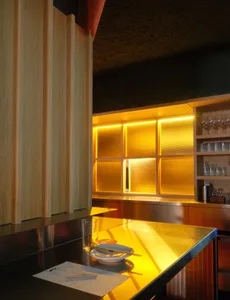 A modern kitchen with a metallic countertop, dining table, and various items, illuminated by a light source, creating a warm and inviting atmosphere