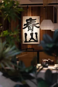 A cozy restaurant with a dining table, chairs, a potted plant, and a large black and white painting on the wall