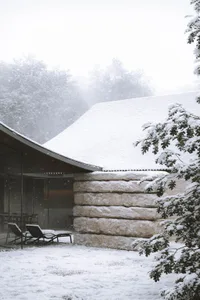 A serene snow-covered house with a curved roof and stone wall, blending modern and traditional architectural styles
