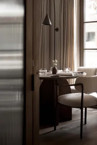 A dimly lit dining room with a wooden table, chairs, and a vase of flowers, set with wine glasses and a bowl