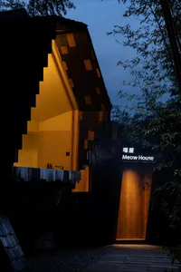 A house with a yellow roof, wooden structure, and large window, illuminated by the house's lights at night