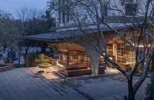 A restaurant with a wooden structure, chairs, and dining tables, lit by evening lighting, creating a cozy and intimate atmosphere