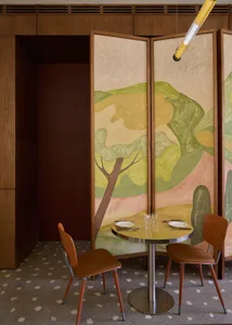 A dimly lit dining area with a wooden table and chairs, surrounded by wine glasses and a painting on the wall, creating a cozy and intimate atmosphere