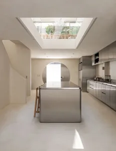 A modern kitchen with a large island, stainless steel countertops, a dining table, and natural light from a window