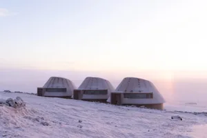 A row of small wooden cabins in a snow-covered landscape, with soft and diffused lighting creating a peaceful atmosphere
