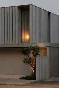 A serene courtyard scene with a concrete building and a small potted tree, bathed in natural sunlight