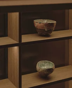 A display case featuring a variety of colorful bowls and vases on wooden shelves with glass surfaces, highlighted by soft lighting