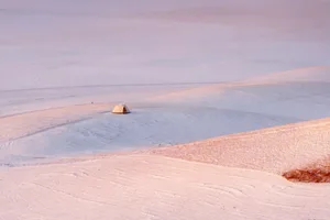 A small tent stands in a snow-covered field, surrounded by a serene and peaceful winter landscape