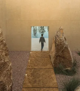 A man walks down a dimly lit hallway lined with large rocks, creating a calm and peaceful atmosphere in a modern building