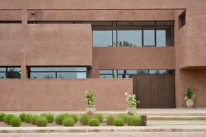 Photograph of a modern building with a concrete facade, a large window, and a door, bathed in natural sunlight