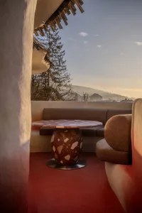 A well-lit living room with a red floor, a couch, a chair, and a dining table, creating a warm and inviting atmosphere