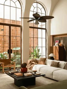 A well-lit living room with a white couch, chair, and dining table, surrounded by furniture and a large fan, creating a comfortable and inviting atmosphere