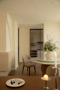 Cozy living room with a wooden floor, a dining table, a couch, and a chair, with a dimly lit atmosphere and a vase with flowers on the table