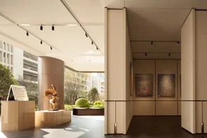 A well-lit modern room with wood, stone, and glass features, adorned with paintings and providing a comfortable space for art appreciation