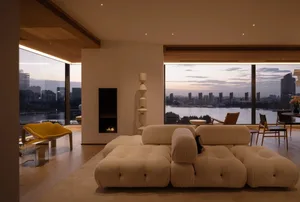 A well-lit living room with a white couch, fireplace, and large window offering a city view