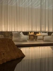 A modern dining space with a wooden table and chairs, surrounded by candles and natural light from a nearby window