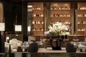 A modern bar area with a large vase of flowers, comfortable seating, and a sophisticated atmosphere, decorated with bottles and a potted plant