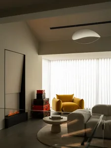 A modern living room with a fireplace, white walls, and a glass table, featuring white furniture and natural light from the windows
