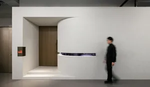 A small, modern room with a white door and wall, open to a bright and clean hallway