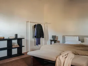 Cozy bedroom with a bed, dresser, and closet, featuring wood and linen/cotton materials, in a neutral color palette with soft warm lighting
