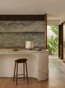Modern kitchen with a white marble countertop, brown stools, and natural light from the windows