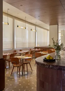 A modern restaurant interior with a dining area and bar featuring wood and marble materials, natural lighting, and a warm atmosphere