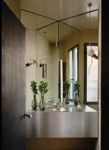 Modern bathroom with a metal sink and large mirror, natural light from a window, and dim lighting creating a cozy atmosphere