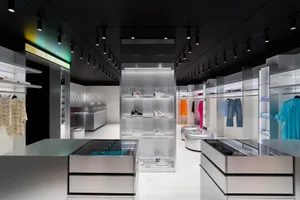 A modern shoe store with a black and white color scheme, featuring a large glass display case showcasing shoes arranged on the floor and shelves, under well-lit conditions