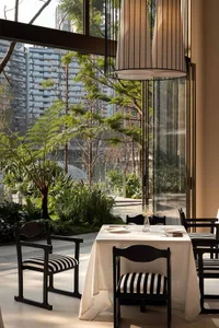 A modern dining area with a wooden table, chairs, and a lamp, set with plates, bowls, and a vase, near a window with natural light