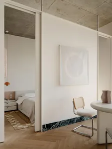 A modern bedroom with a white color scheme, a marble countertop, and a bed positioned against the wall, accompanied by a chair and a table in a functional arrangement