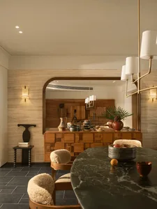 A modern kitchen with a black marble countertop, wooden cabinets, and a cozy atmosphere created by dim lighting, featuring a dining table, chairs, and various decorative items