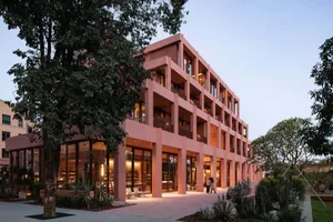 A modern hotel building with a pink and brown color scheme, featuring a courtyard and patio area, with natural light and inviting atmosphere