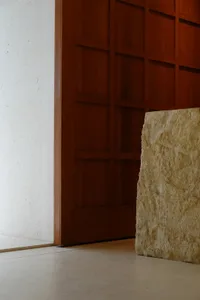 A dimly lit room with a wooden floor and a large natural stone rock in front of a wooden doorway