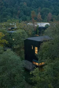 A serene black house surrounded by green trees, with a wooden deck and natural sunlight shining on the scene