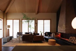 A well-lit living room with a brown couch, a chair, and a potted plant, set against a wooden floor and a dining table