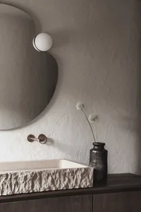 A modern bathroom with a sink, mirror, and vase with a flower, set against a bright and inviting background
