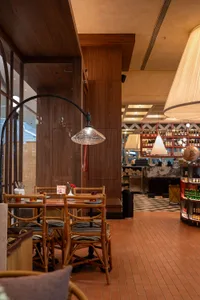 A well-lit restaurant interior with wooden furniture, tables, chairs, and a bar, featuring a modern and contemporary atmosphere