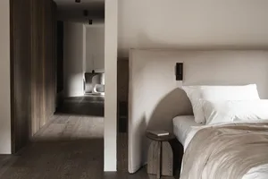 Cozy bedroom with a bed, chair, and bench, dimly lit with a simple and functional style