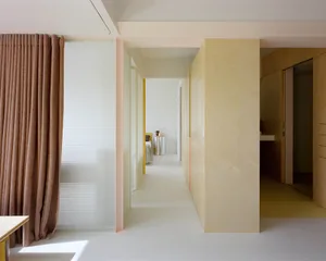 A dimly lit modern hallway with pink and white accents, white walls, and a wooden floor, featuring a doorway at the end