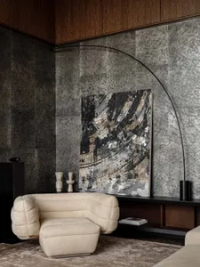 A well-lit living room with a white couch, a chair, a large painting, and two vases on a table, creating a warm and inviting atmosphere