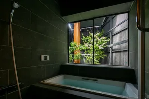 Bathroom with a black and white color scheme, featuring a bathtub with a window above it, allowing natural light to enter the room, with a tree visible outside