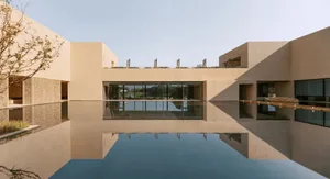 A modern building with a reflecting pool in front, featuring brown and white colors, set in a sunny day with clear reflections in the water