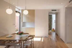A modern kitchen and dining area with a wooden table, chairs, and cabinets, surrounded by a cozy atmosphere and natural light